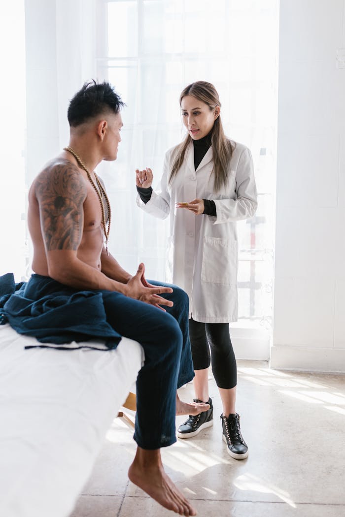Female doctor consults with tattooed male patient indoors in bright room.